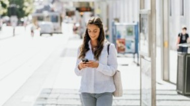 Frau mit Smartphone an Haltestelle