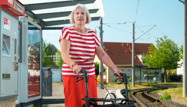 Rentnerin mit Rollator an Haltestelle