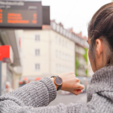 Frau steht an Haltestelle und schaut auf Armbanduhr