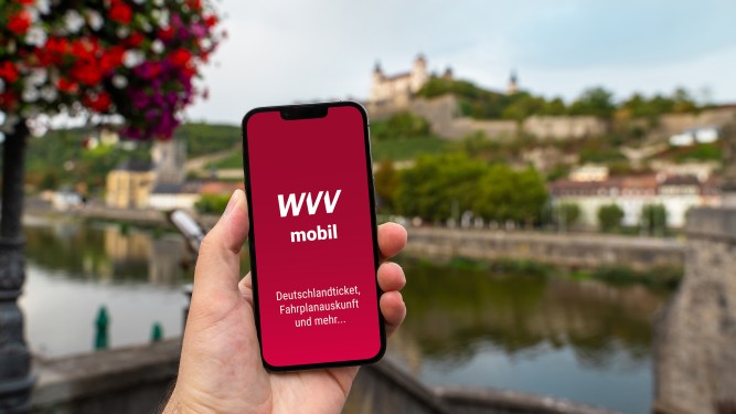Hand, die Handy mit WVVmobil-App hält, im Hintergrund Festung von Würzburg